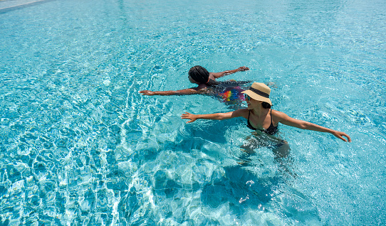 Two women swim happily in clear blue water of a swimming pool on a sunny day.
