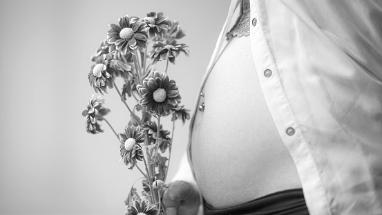 Pregnant belly. Closeup of pregnant belly in black and white with flowers. Pregnant woman holding a bouquet of flowers in front of her belly in first months of motherhood