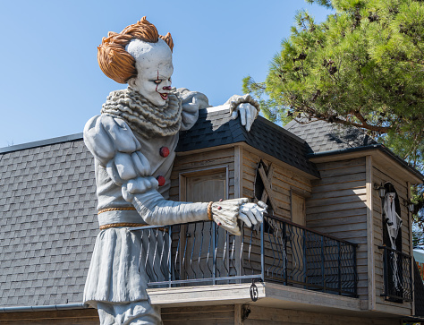 House of fear. Figure of huge clown with red hair and white face. Right hand holds railing of balcony of two-story house. Left hand lies on roof of House of Fear. Gelendzhik, Russia – September 27.