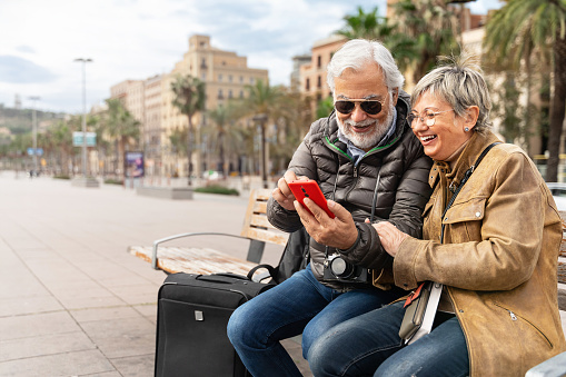 Active senior couple tourists traveling together using cell phone to check hotel restaurant direction