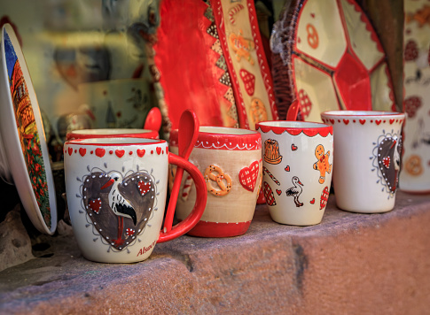 Riquewihr, France - June 2 2023: Ceramic mugs with traditional Alsatian designs, storks, gingerbread man and pretzels on display at a souvenir store