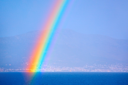 Rainbow over the sea and coastal city and mountains in the background