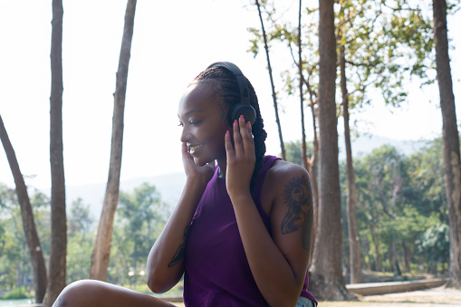 Young African American woman in the park listening to the music. Black woman listening to music on her headphones in the local park during spring season for resting and relaxing by looking out into beautiful landscape with positive emotion.