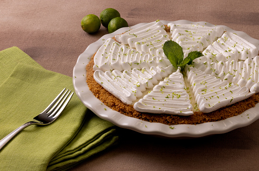 Key lime pie with decorative meringue in a white ceramic pie plate and green napkin and fork