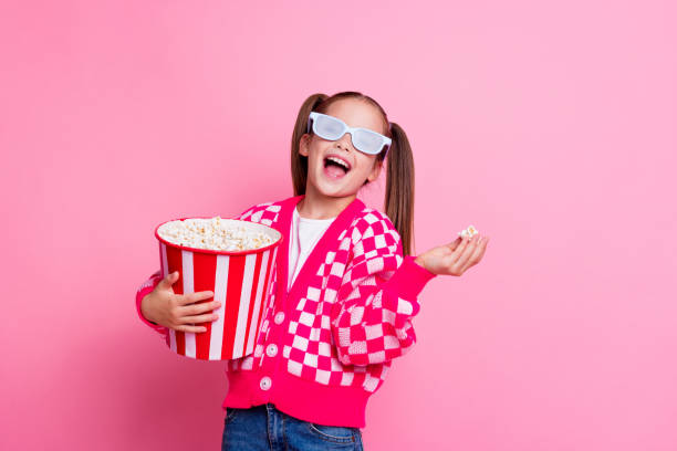 foto de menina alegre bonito usar roupas da moda comer pipoca saborosa assistindo filme de desenho animado espaço vazio isolado no fundo da cor rosa - film tails - fotografias e filmes do acervo