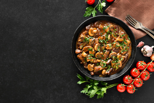 Tasty beef stroganoff with mushrooms in frying pan over black stone background with copy space. Top view, flat lay