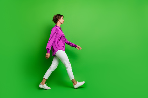 Profile side full length photo of adorable cute stylish girl walking moving looking empty space isolated on green color background.