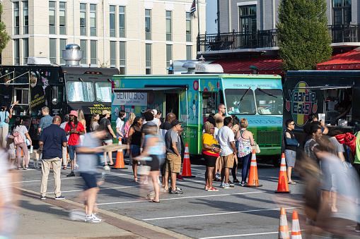 Suwanee, GA / USA - August 4, 2023:  People motion blur while buying meals from food trucks at an event on August 4, 2023 in Suwanee, GA.