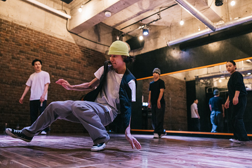 Japanese man showing hip hop moves, while doing dance battle with friends in a studio.