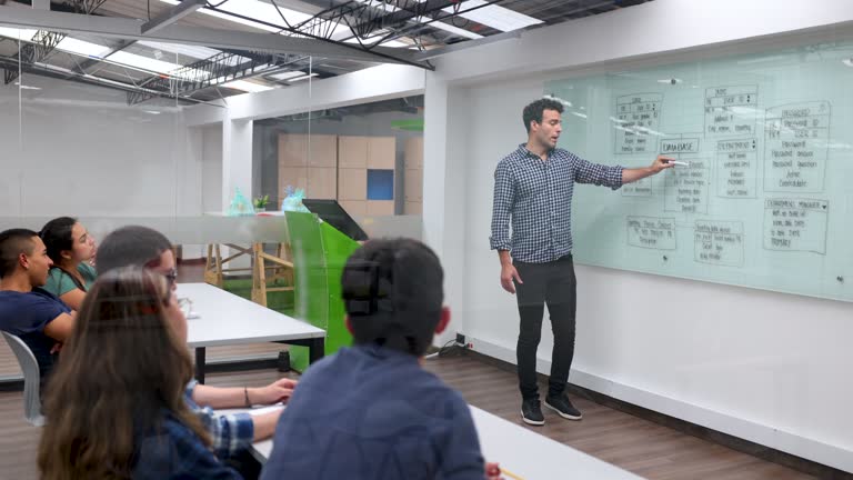 Latin American teacher giving an IT lesson and explaining a user experience diagram on the board to a group of students