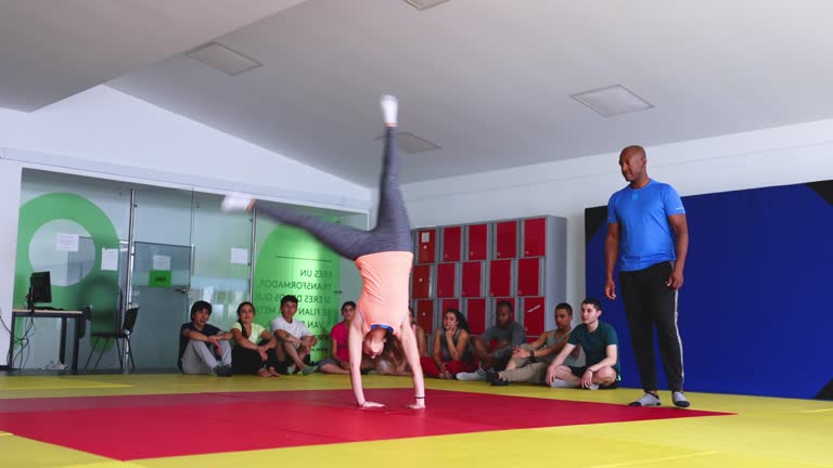 University student in physical education class doing a cartwheel in front of her teacher