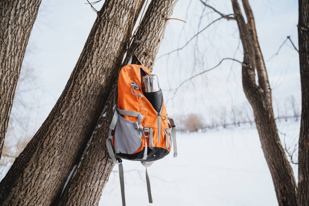 istock Bright orange backpack hanging on a tree in the woods, silver thermos bottle in side pocket 2007866295