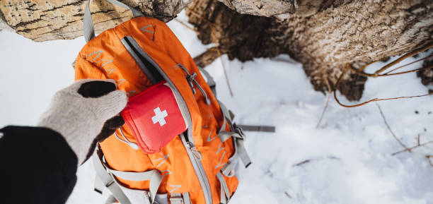 istock Hand grabbing first aid kit from orange backpack in snowy forest. Emergency preparedness concept. 2007869565