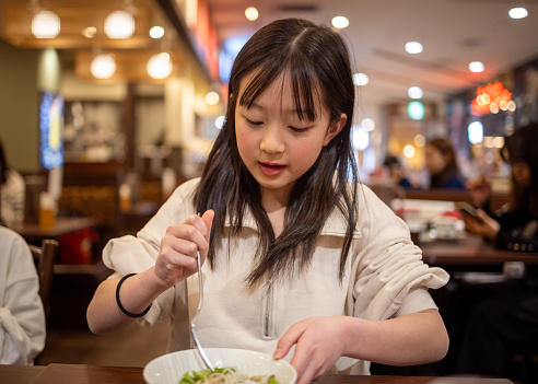Teenage girl eating pasta for lunch in restaurant