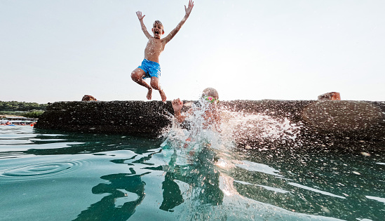 Young happy couple have fun at sea beach. Children run, jump high into water. Popular travel destination. Family summer vacation with kids at tropical island.