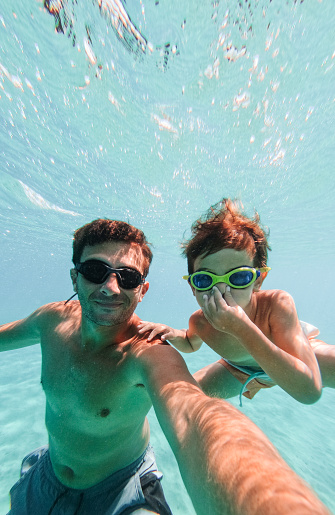 Photo of cute little boy and his dad making underwater selfie