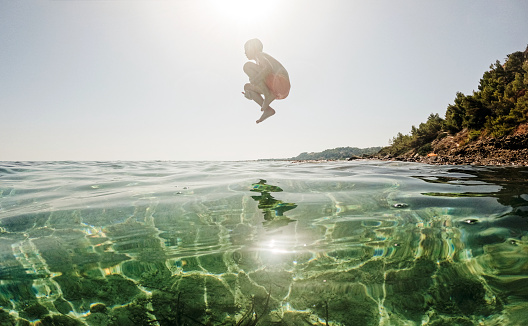 Photo of an adventurous young boy jumping off a big rock into the sea