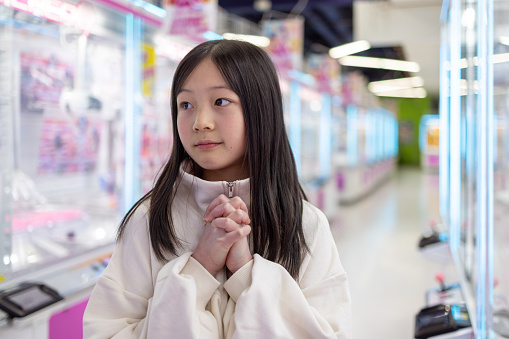 Teenage girl praying for success in front of crane game in amusement arcade