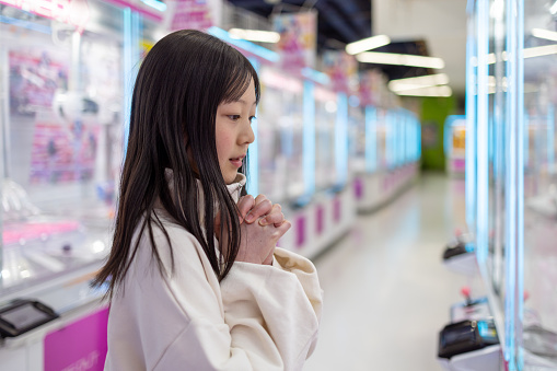 Teenage girl praying for success in front of crane game in amusement arcade