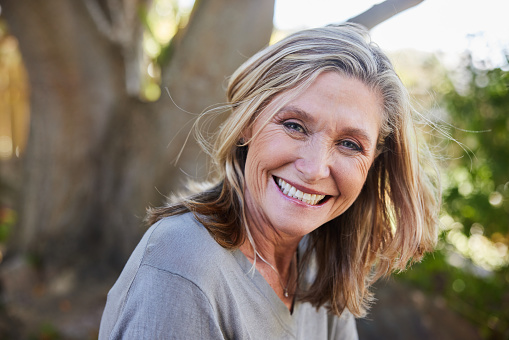 Portrait of a mature woman smiling while sitting alone outside in her back yard at home in summer