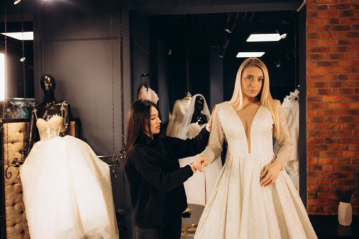 Bride at the clothes shop for wedding dresses; she is choosing a dress and the designer is assisting her. High quality photo