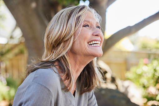 Carefree mature woman laughing while relaxing alone outside in her back yard at home in summer