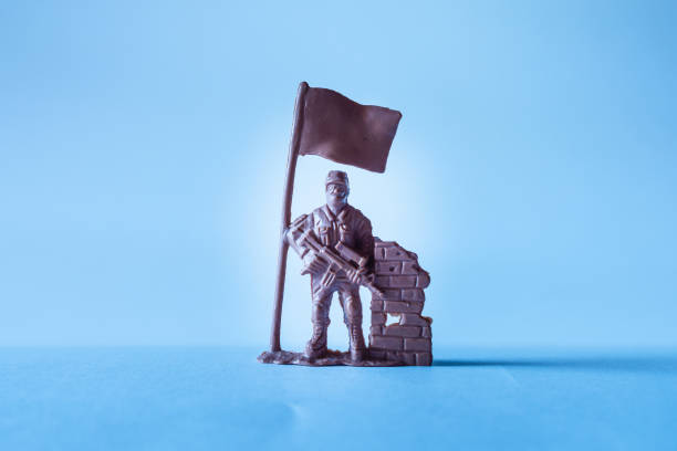 Miniature toy soldier,holding flag,stands on a dramatic overcast blue background.Copy space.Indoors shot.