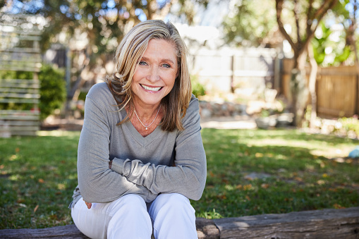 Portrait of a mature woman smiling while sitting on a stone step outside in her back yard at home in summer