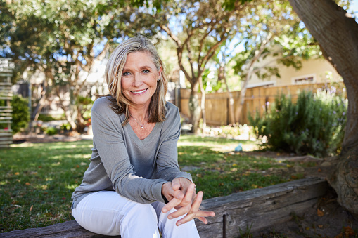 Portrait of a mature woman smiling while sitting on a stone step outside in her back yard at home in the summer time