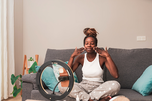 african american Content Creator woman Applying Skincare Products on Face during online tutorial session at Home