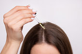 A young woman applies a drop of oil from a pipette to her scalp, close-up