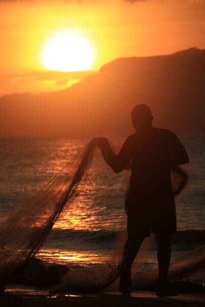 Banda Aceh, 12/14/2019, Fishermen are repairing their fishing nets on the beach at sunset. In the reddish-orange glow of twilight, they diligently clean the nets from the day's catch. A peaceful atmosphere is created amidst the shimmering sea, while the sky welcomes the night with captivating warmth