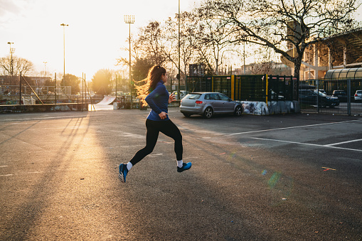 A woman is running in the city at sunset. She's running in a parking lot.