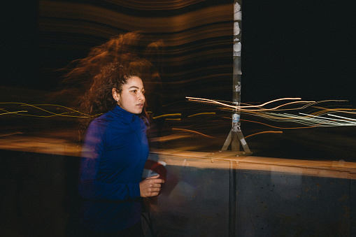 A woman is running in the city at night. Creative effect from the light trails of the street lights.