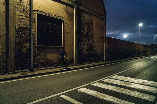 A woman is running at night in the city. She's running on the sidewalk.