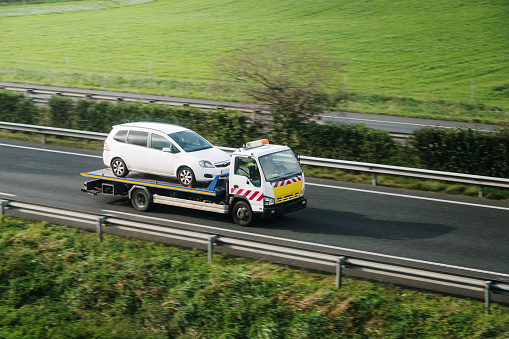 A tow truck carrying a broken down car on a highway