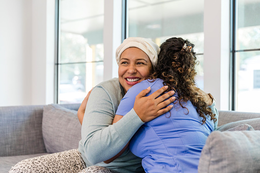 The female cancer patient smiles while giving her hospice nurse a hug.