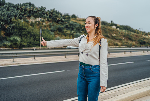 Cheerful young woman hitchhiking on a highway in Malta