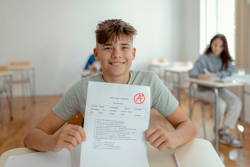 Portrait of teenager looking at camera while sitting in classroom with perfect grade a plus test results. Childhood, education and people concept