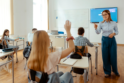 Student raising hand while teacher teaching in classroom