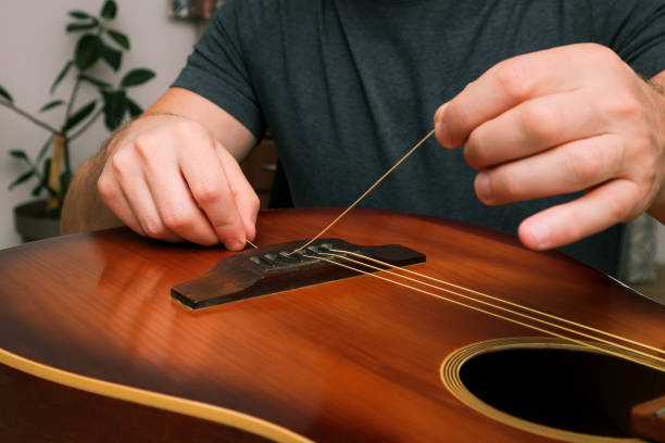 istock Hands of a young man changing the string on an acoustic guitar. Hand fixing guitar. 2008057543