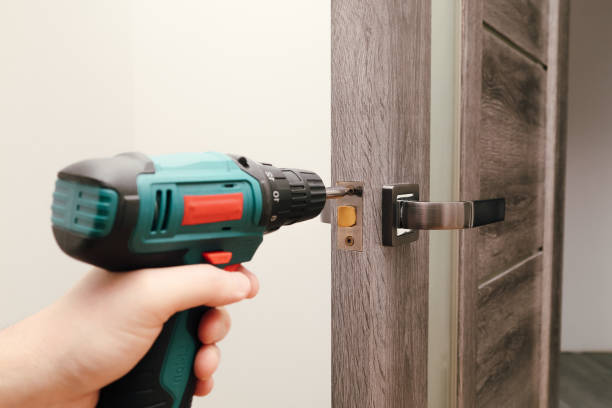 istock Handyman Fitting A New Door Using A Screwdriver At Home. Carpenter at lock installation with electric drill into interior wood door 2008058135