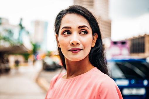 Attractive fashionable woman in the streets of downtown Kuala Lumpur. Looking around, turning her head with a slight smile while crossing the city street. Selective Focus, Soft Bokeh. Natural Female Urban City Portrait. Kuala Lumpur, Malaysia, Southeast Asia