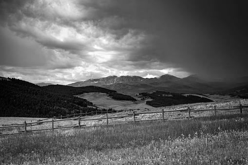 Retro monochrome summer landscape of dark storm clouds, mountains, valley, evergreen forest and wood fence in the Bighorn Mountains Recreation area of Wyoming, USA