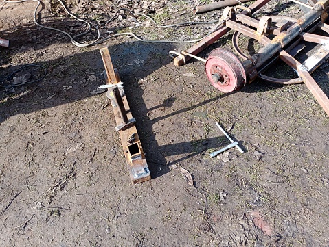 Repair of a horse carriage. In the photo, a beam without wheels is lying on the ground next to a mechanical key. Repair of public transport.