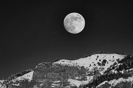 Full moon rising in a cloudless sky over Carter Mountain during winter in the Wyoming Rocky Mountains, USA