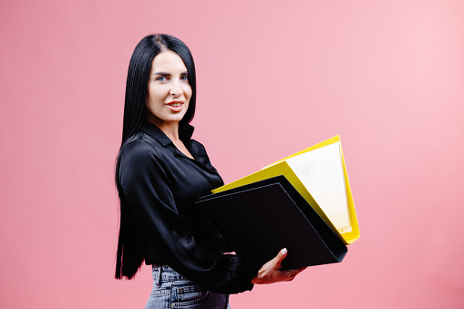 Young successful employee business secretary woman wearing in classic black shirt, working in office with folders for papers and documents, bookkeeping isolated on pink background studio.