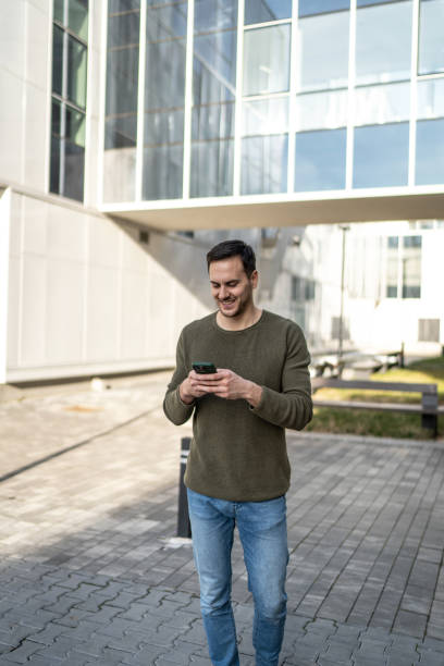 街でスマートフォンを使う若いハンサムな男。携帯電話でメールを打つ笑顔の学生男性 - single line urban scene outdoors vertical ストックフォトと画像