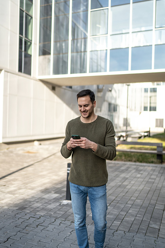 Young handsome man using smartphone in a city. Smiling student men texting on his mobile phone