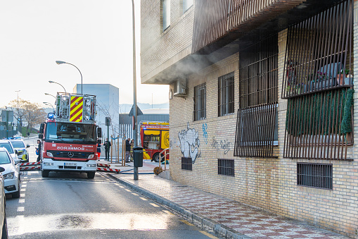 Granada, Spain; 2024, February - 1: Fire crew at work outside a smoke-filled apartment, with firefighting equipment in view.